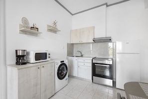 A compact kitchen with a washing machine, microwave, oven, and a coffee maker. - Sun & Beach Apartment in Chania 14 (Chania)