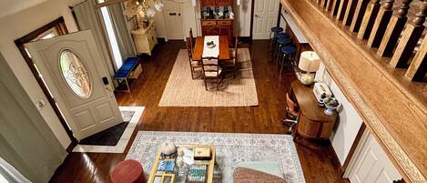 A spacious living area with a high ceiling, a dining table, a sofa set, and a staircase.