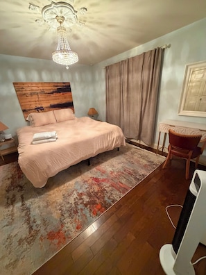 A bedroom with a large bed, a wooden headboard, a chandelier, a desk with a chair, and a window with curtains. - Anchor Down by the Bay,  A Restful Retreat   in Lewes (Lewes)