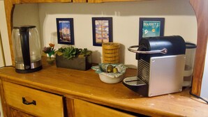 Een aanrecht met een koffiezetapparaat, een waterkoker, een plant en fotokaders aan de muur.