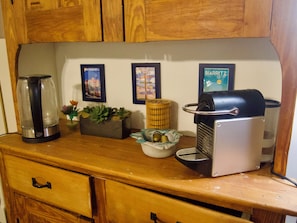 A kitchen counter with a coffee maker, a kettle, a plant, and framed pictures on the wall.
