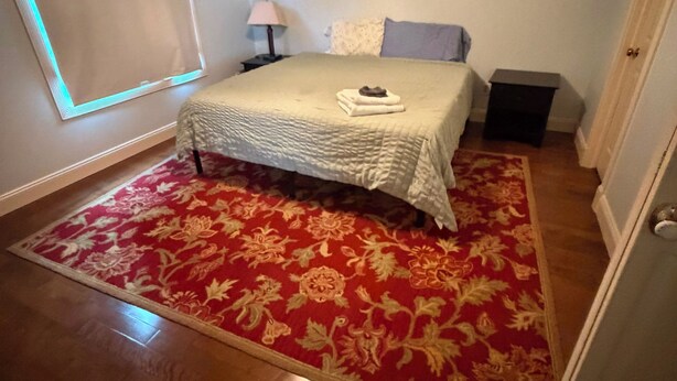 Een slaapkamer met een bed, een plafondventilator, een nachtkastje, een lamp en een raam.