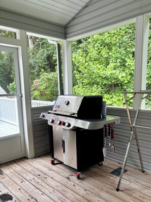 A covered porch with a stainless steel grill, a ladder, and a view of a wooden deck and greenery. - Anchor Down by the Bay,  A Restful Retreat   in Lewes (Lewes)