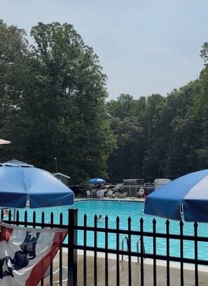 Une piscine entourée d’une clôture, bordée d’arbres et agrémentée de parasols.