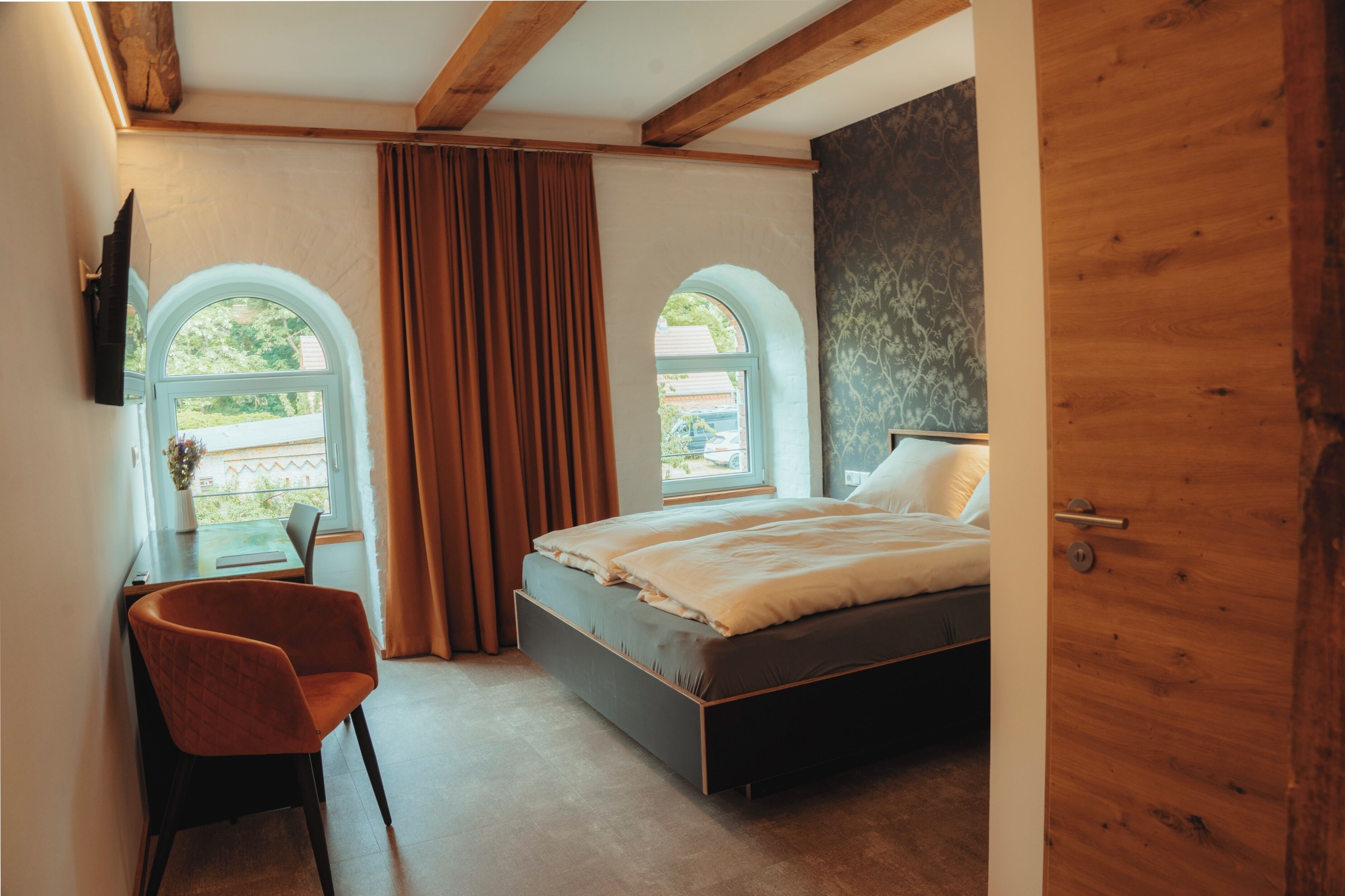 Une chambre à coucher avec un lit, une chaise, un bureau et deux fenêtres.