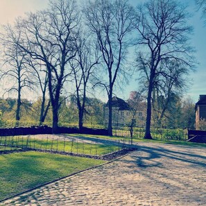 A cobblestone pathway leading through a park with bare trees and a distant building.