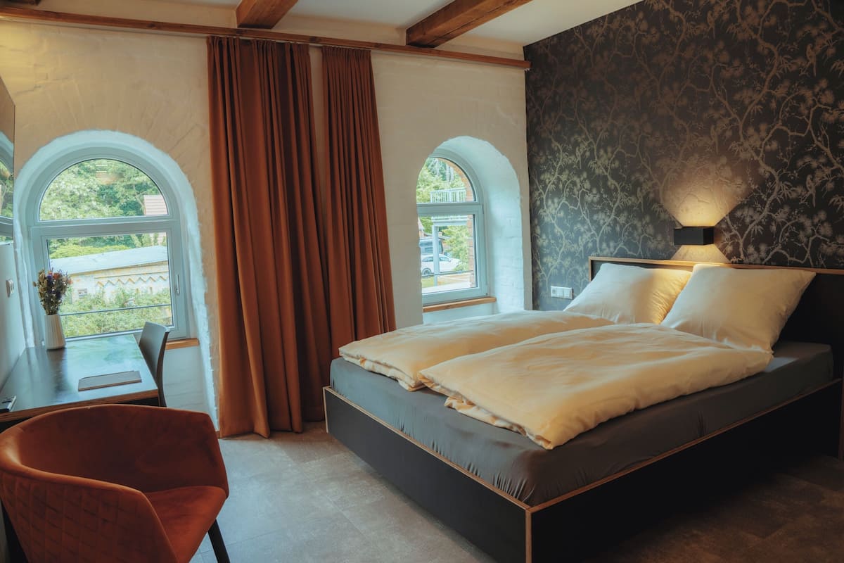 A bedroom with a bed, two windows, a desk, and a chair.