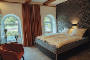 A bedroom with a bed, two windows, a desk, and a chair.