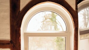A room with a large arched window, a wooden chair, and a table.