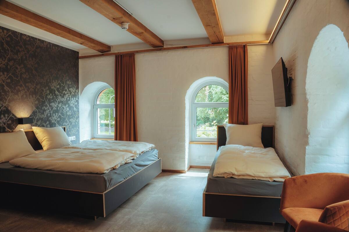 A bedroom with two beds, a wooden ceiling, a large window, and a wall-mounted TV.