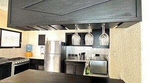 A kitchen with a black countertop, stainless steel appliances, and hanging wine glasses. - Incredible house with pool and garden (Cancún)