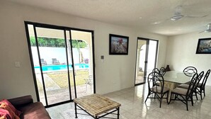 A spacious living area with a large sliding glass door leading to a pool, a dining table with chairs, and a ceiling fan. - Incredible house with pool and garden (Cancún)