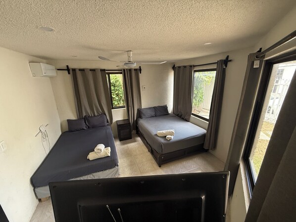 Ein Zimmer mit zwei Betten, einem Deckenventilator und einem Fenster mit Vorhängen.