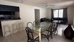 A modern living space with a glass dining table, dark chairs, a sofa, a large vase, and ceiling fans. - Incredible house with pool and garden (Cancún)