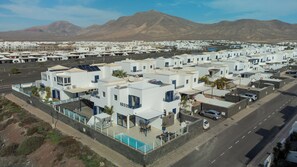 A residential area with white buildings, a swimming pool, and a mountain in the background. - Villa Kalandraka Pool, Sea Views, 10 min to Marina (Playa Blanca)