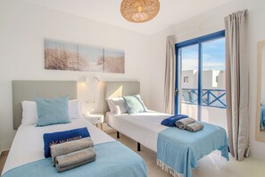 Ein Hotelzimmer mit zwei Betten, einem großen Fenster mit Ausblick, einer Deckenleuchte und einem an der Wand befestigten Kunstwerk.