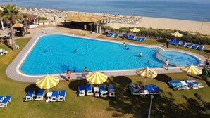 Une piscine dotée de chaises longues et de parasols, entourée d’un espace paysager offrant une vue sur la mer.