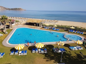 A swimming pool with lounge chairs and umbrellas, surrounded by a landscaped area with a view of the sea.
