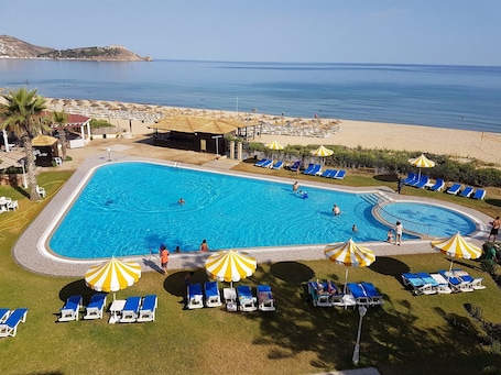 Una piscina con sillones de descanso y sombrillas, rodeada de un área ajardinada con vista al mar.. Mehari Tabarka