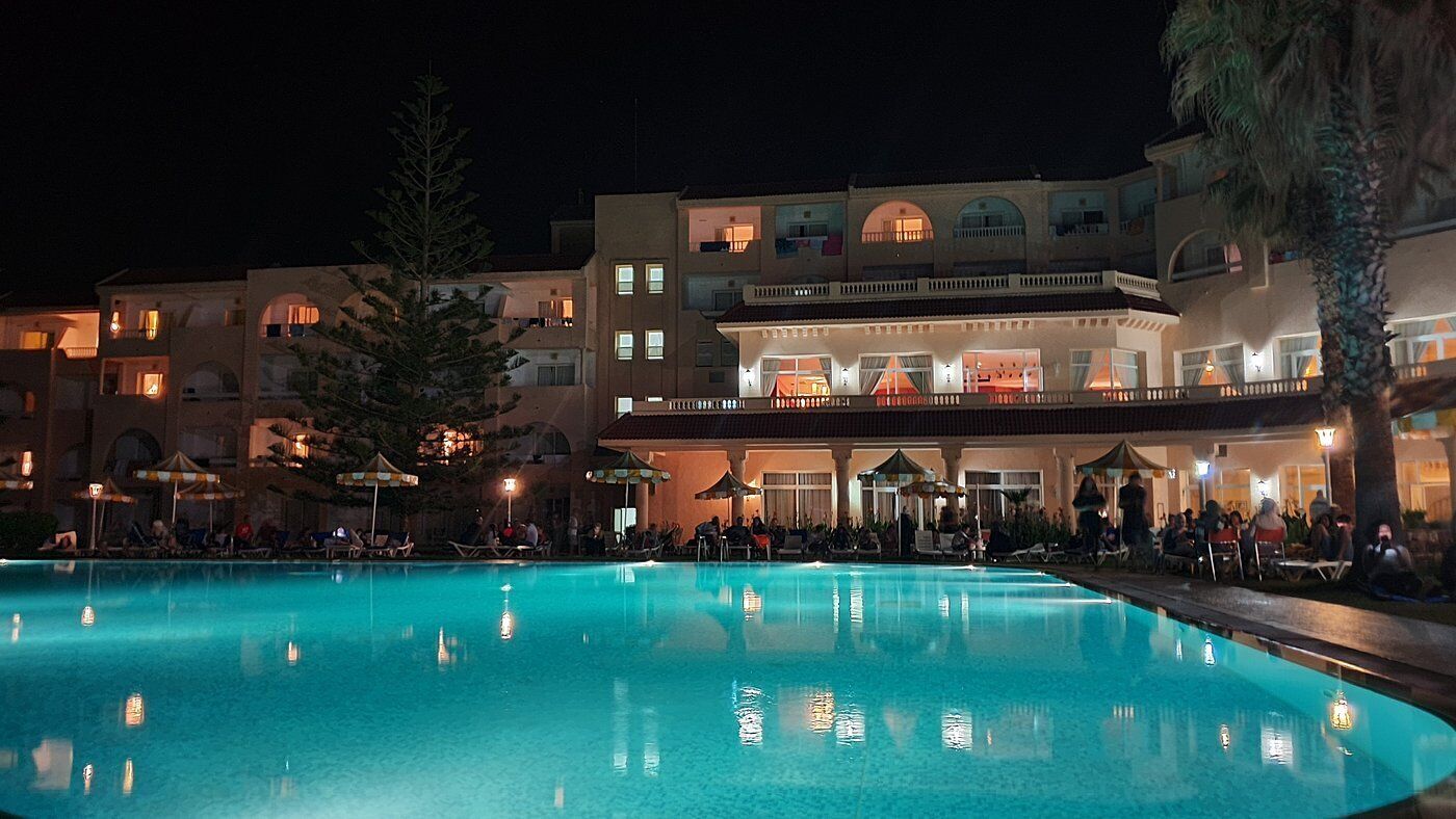 A hotel with a swimming pool, outdoor seating, and multiple balconies.