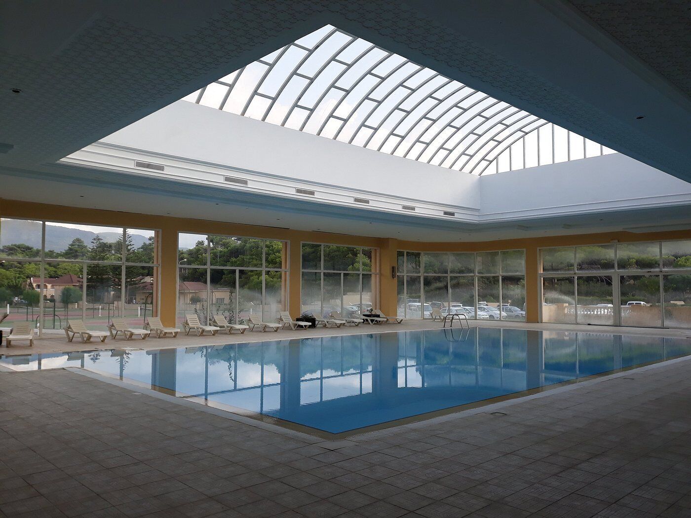 Una piscina interior con tragaluces, vistas despejadas al exterior y sillas de descanso.