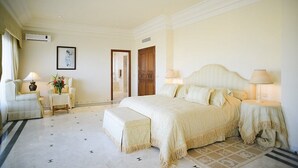Une chambre d’hôtel avec un grand lit, deux tables de chevet avec des lampes, une chaise, une petite table avec des fleurs et un tableau encadré au mur.