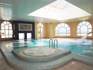 Une piscine intérieure dotée d’un jacuzzi, de fenêtres en arc de cercle et d’une verrière.