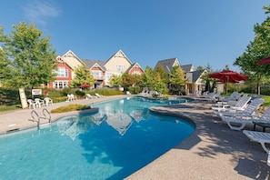 A swimming pool with lounge chairs and umbrellas, surrounded by buildings with a traditional architectural style. - Ski & Tee Retreat - Walk to Village (The Blue Mountains)