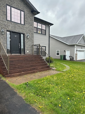 A two-story house with a stone facade, a black front door, and a set of wooden stairs leading to a porch.
