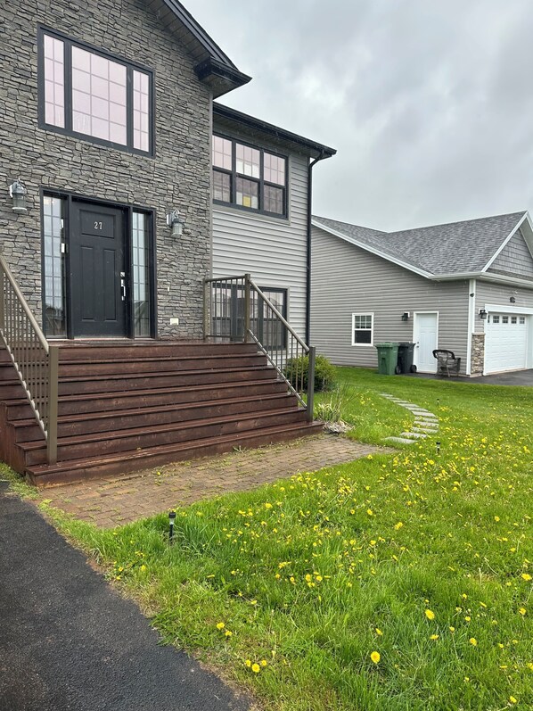 A two-story house with a stone facade, a black front door, and a set of wooden stairs leading to a porch.