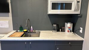 Une cuisine équipée d’un four à micro-ondes blanc, d’un évier en acier inoxydable et d’une machine à café Keurig.