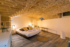 Une chambre avec un plafond en pierre, un lit avec des oreillers, une table de chevet, une petite table et un radiateur.
