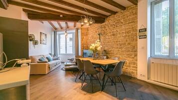 Un salon chaleureux avec un mur en pierre, des poutres apparentes en bois au plafond, une table à manger avec des chaises et un canapé.