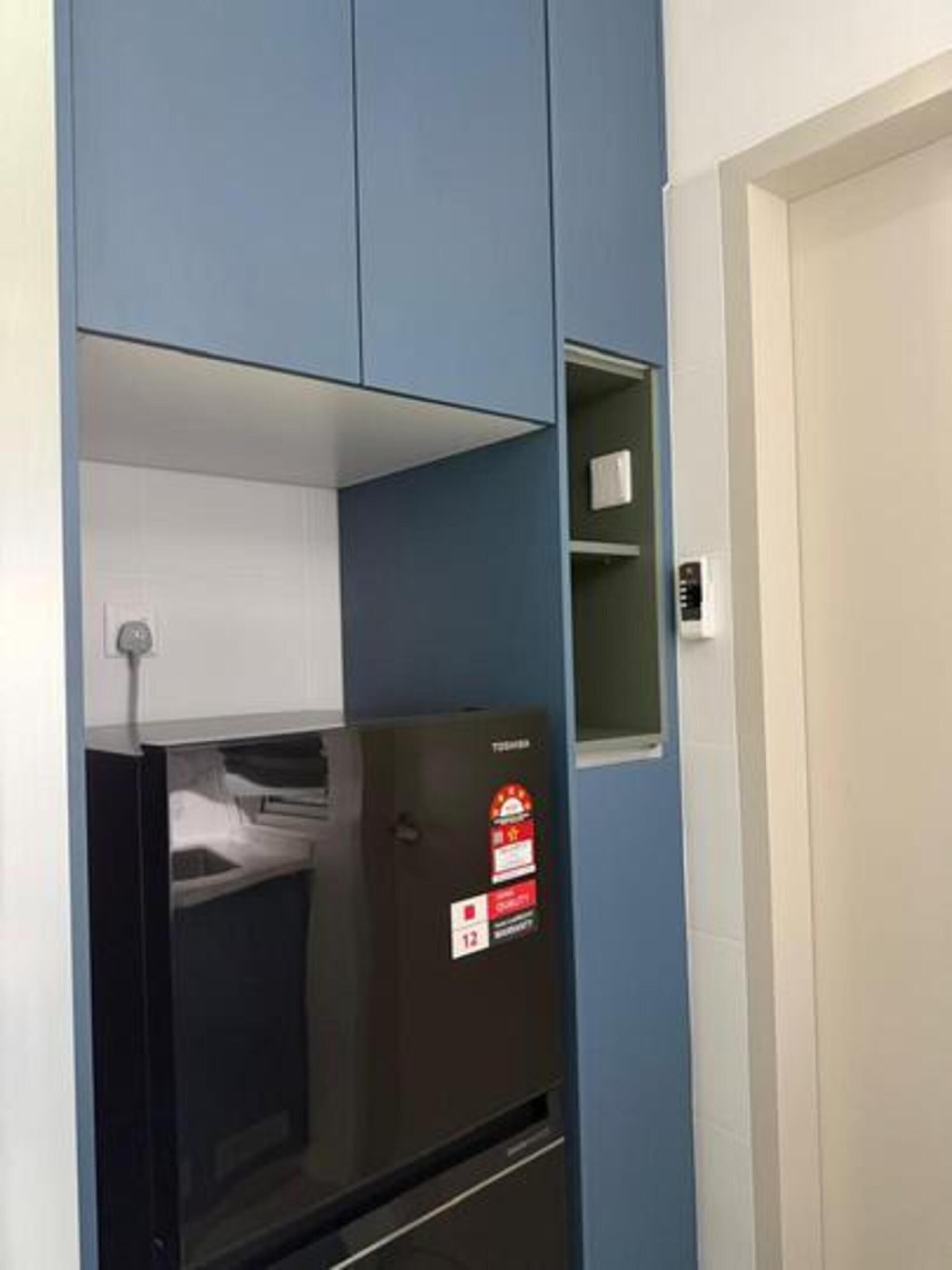Une pièce avec un réfrigérateur noir, une petite étagère et une porte blanche.