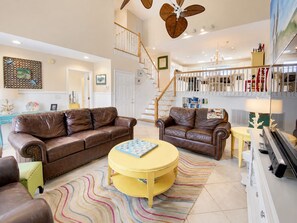 Ein geräumiges Wohnzimmer mit Ledersofas, einem runden gelben Couchtisch und einer Treppe, die in einen oberen Bereich führt.