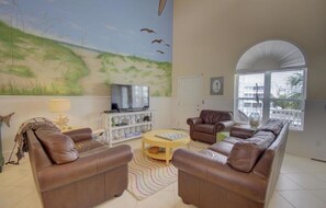 Ein Wohnzimmer mit großem Fernseher, Ledersofas, einem Couchtisch und einem Wandgemälde von Vögeln.