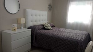 A bedroom with a bed, a nightstand, a chair, a dresser, a mirror, and a window with curtains. - Casa Marconi de Conil (Conil de la Frontera)