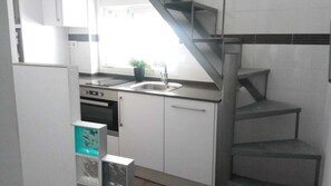 Eine Küche mit weißen Schränken, einem Spülbecken, einem Herd und einer Treppe.