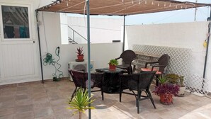 An outdoor patio with a table and chairs, potted plants, and a white wall in the background. - Casa Marconi de Conil (Conil de la Frontera)