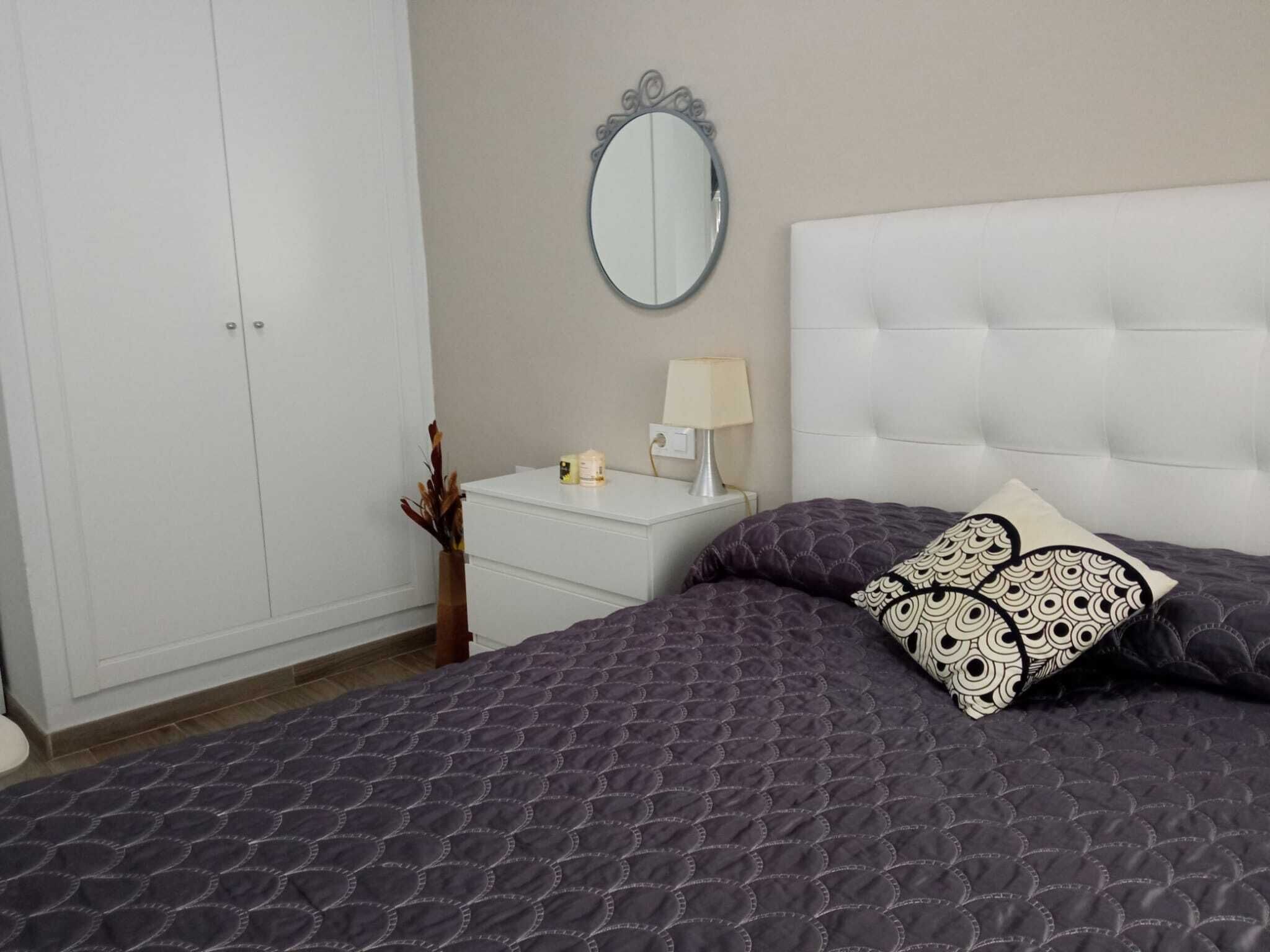 Un dormitorio con cama, mesita de noche, espejo y armario.