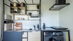 Ett kompakt kök med tvättmaskin, kaffebryggare och en bärbar dator på bänkskivan.