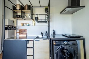 A compact kitchen with a washing machine, a coffee maker, and a laptop on the counter. - Warrina Retreat Parkside Serenity near Urban Life (Chatswood West)