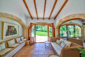 A spacious room with a stone floor, a wooden ceiling, and a large window offering a view of a garden. - Casa Violeta — Mediterranean Art Villa in Jávea (Xàbia)