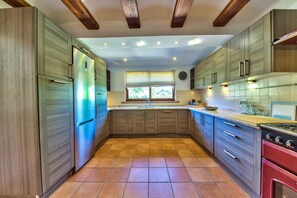 Eine Küche mit Holzausstattung, einem Edelstahlkühlschrank, einem roten Backofen und einem Fenster mit Jalousien.