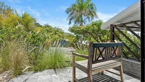 A wooden bench on a stone patio with a view of a garden and a building in the background. - NAYA (Saint-Martin)