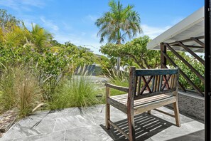 A wooden bench on a stone patio with a view of a garden and a building in the background. - NAYA (Saint-Martin)