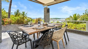 An outdoor dining area with a wooden table, black chairs, and a stone pillar. - NAYA (Saint-Martin)
