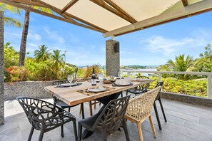 An outdoor dining area with a wooden table, black chairs, and a stone pillar. - NAYA (Saint-Martin)