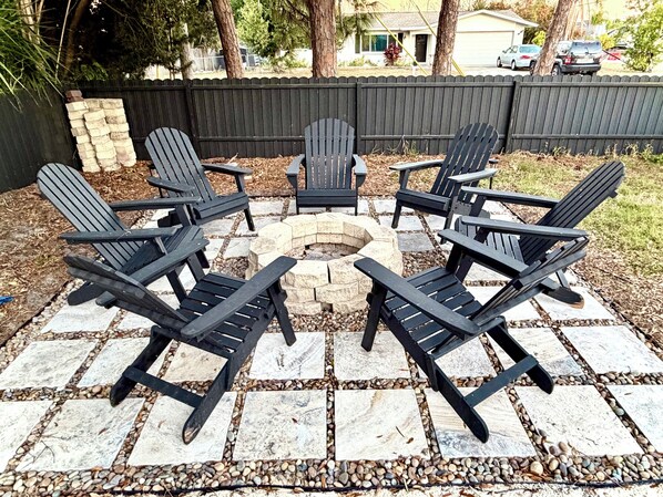 Eine Terrasse mit vier Adirondack-Stühlen, die um eine Steinkaminfeuerstelle angeordnet sind.
