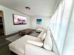Ein Wohnzimmer mit Ecksofa, Couchtisch, Flachbildfernseher und zwei gerahmten Bildern an der Wand.